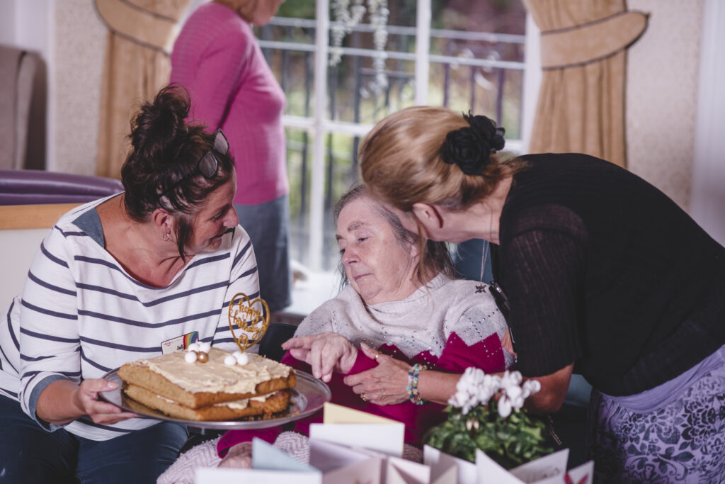 A Sefton Hall care home resident is presented with a birthday cake by two members of the team.