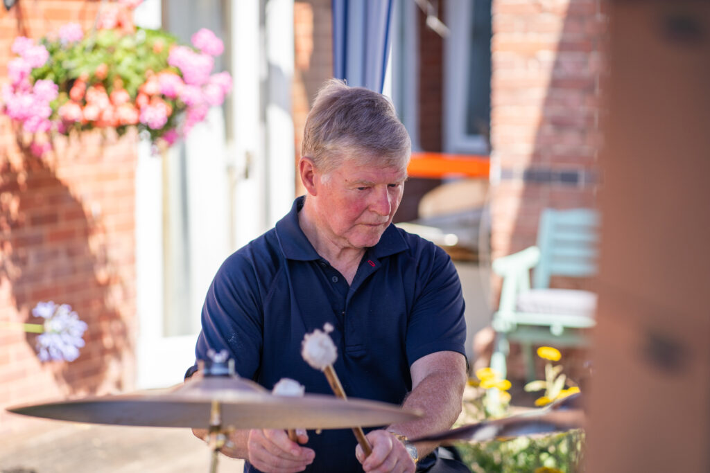 Geoffrey Cox plays the drums in the Southern Healthcare house band. He is performing outside in the Old Rectory Garden. He is a passionate about the positive impacts on wellbeing of live music in care homes. 