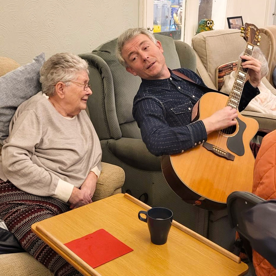 George Williams, Southern Healthcare's resident musician, plays the guitar and sings with a resident in the lounge of the care home. He plays live music in care homes across Devon.