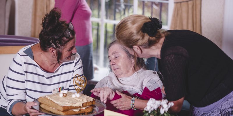 A Sefton Hall care home resident is presented with a birthday cake by two members of the team.
