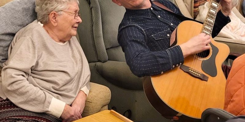 George Williams, Southern Healthcare's resident musician, plays the guitar and sings with a resident in the lounge of the care home. He plays live music in care homes across Devon.